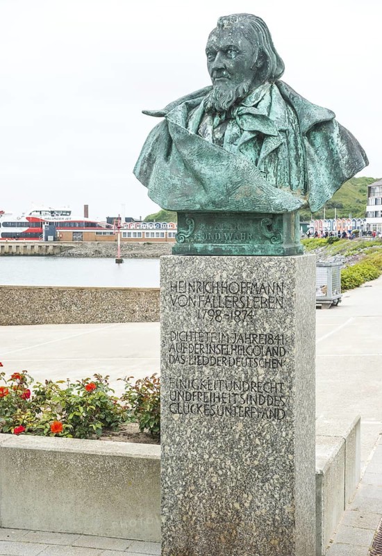Sculpture, monument, bust, bronze bust of August Heinrich Hoffmann von Fallersleben, author of the later German national anthem, Das Lied der Deutschen, on a stone pedestal with a view of the sea in the background the North Sea, the Halunderjet in the harbour and the lobster shacks, colourful, brightly coloured buildings, writer, poet, unity and justice and freedom, Helgoland spa promenade, Schleswig-Holstein, Germany