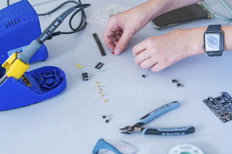 Working with electronic components on a table, soldering iron and hands clearly visible