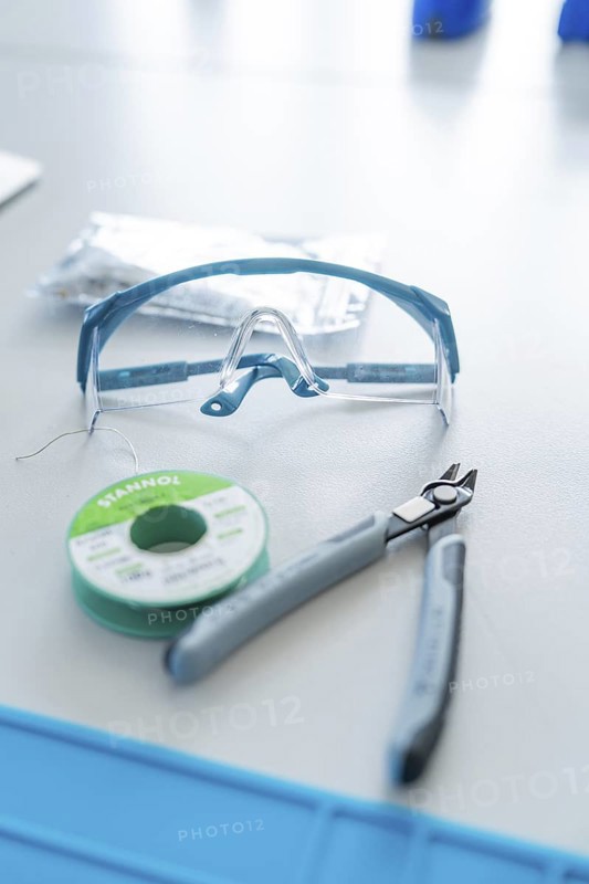 Safety goggles, pliers and solder on a table for electronics work