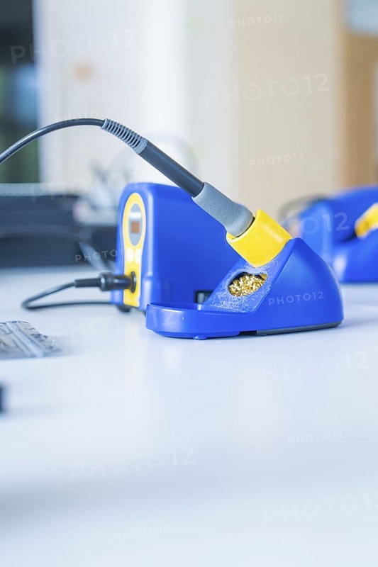 Close-up of a blue soldering iron on a workshop table with blurred background