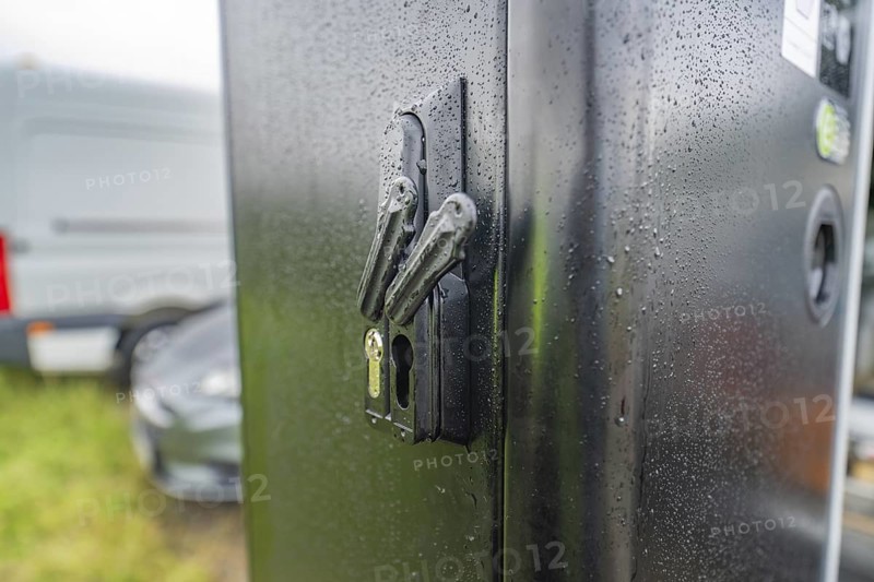 Security lock on a rain-soaked, black housing next to a parked car, installation of a charging station for electric cars, Calw, Germany