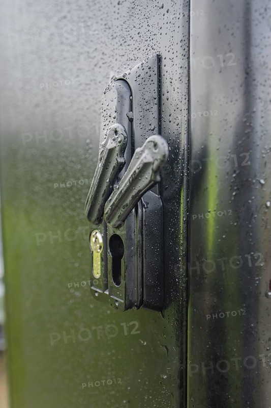 Wet lock on a black door with visible water droplets and reflected light, installation of a charging station for electric cars, Calw, Germany