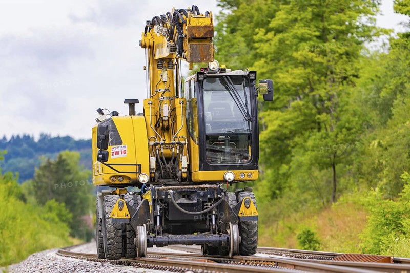 Large yellow construction machine on rails, surrounded by trees and greenery, grinding work on the Hermann Hesse railway, Ostelsheim, district of Calw, Germany