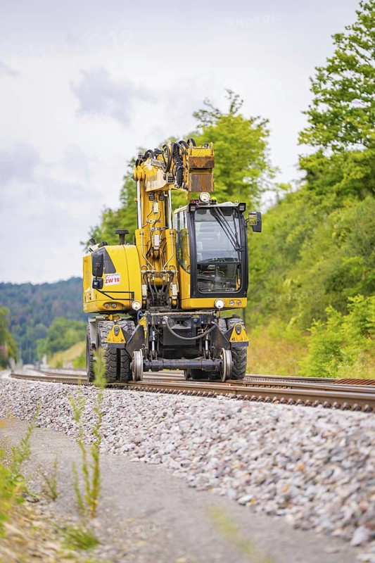 Yellow railway crane on railway tracks, surrounded by trees and ballast, grinding work on the Hermann Hesse railway, Ostelsheim, district of Calw, Germany