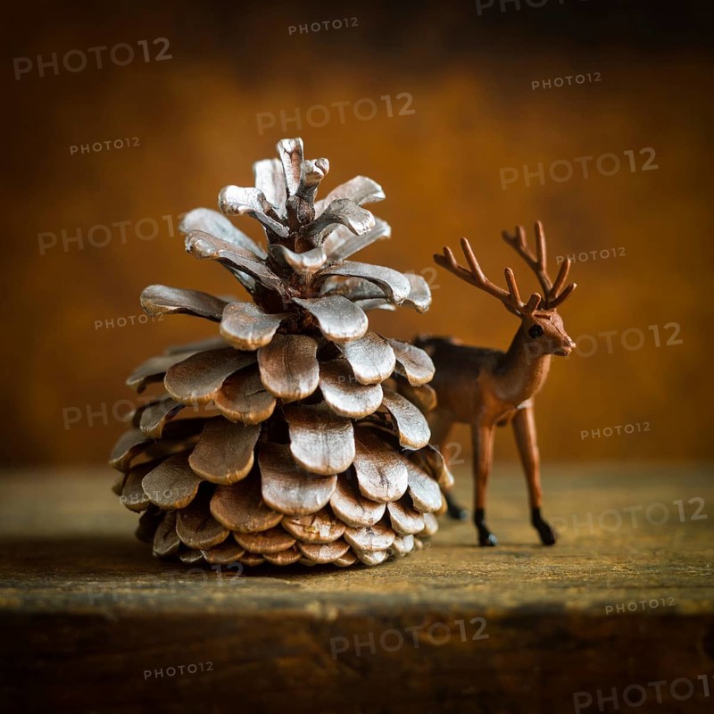 A charming deer figurine stands next to a large pine cone, evoking a cozy winter ambiance. This arrangement is perfect for holiday decor, adding a touch of nature