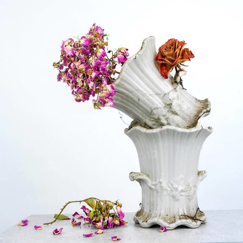 Dried flowers with rich colors are placed in a vintage white vase, showcasing elegance and nostalgia in a minimalist setting. The table beneath adds a touch of simplicity to the arrangement
