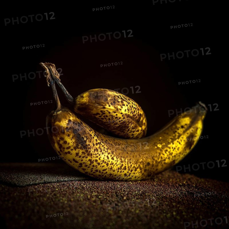 Two ripe bananas, one larger and one smaller, showcase their dark speckled skins. Positioned on a textured surface, they contrast beautifully against the deep black background