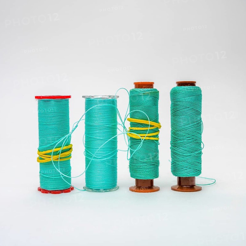 A collection of turquoise bobbins of thread is displayed, showcasing different sizes and textures