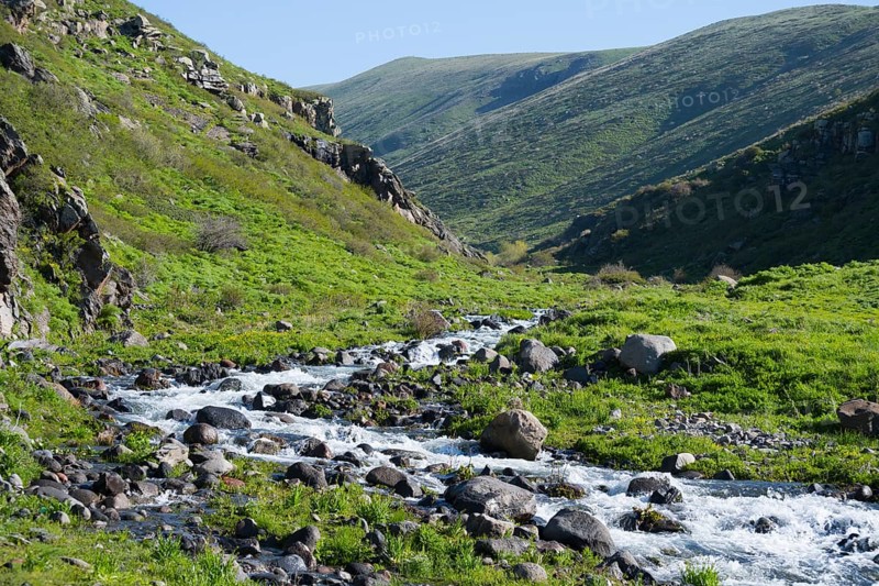 Clear mountain river snakes through a green valley between stony slopes, Amberd Gorge, Aragazotn Province, Armenia
