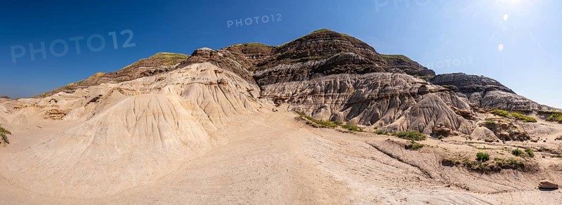 Breathtaking panorama showcasing unique geological formations, known as hoodoos, rising from arid terrain in drumheller, canada, bathed in sunlight against a vibrant blue sky