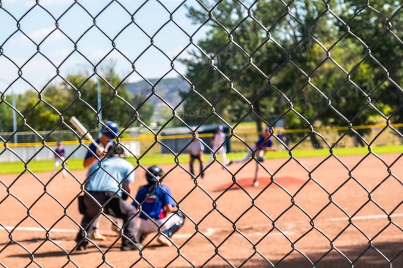 Blurred baseball players competing in a youth game, seen through a chain link fence, showcasing the spirit of competition and the timeless appeal of the sport