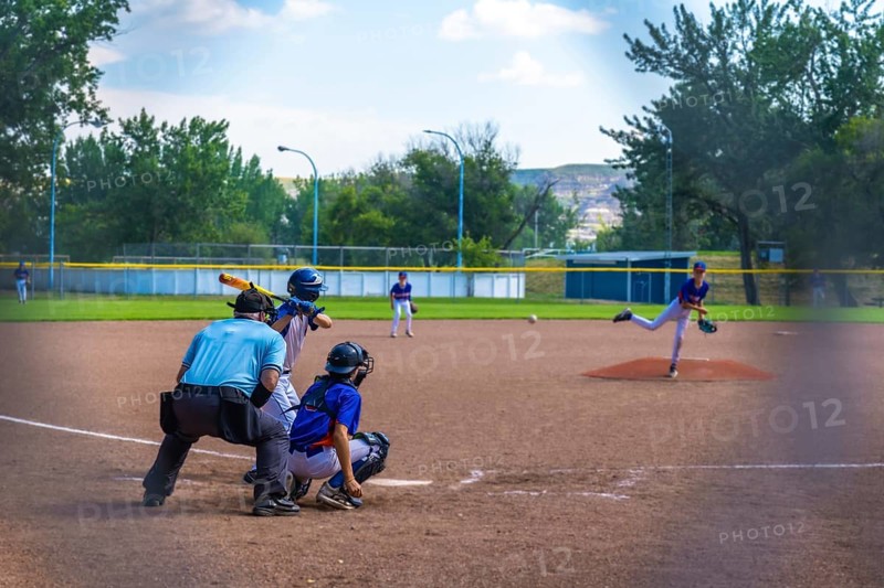 Young baseball pitcher throwing a ball during an intense game, while the batter, catcher, and umpire watch closely under the bright sun on a lively summer day