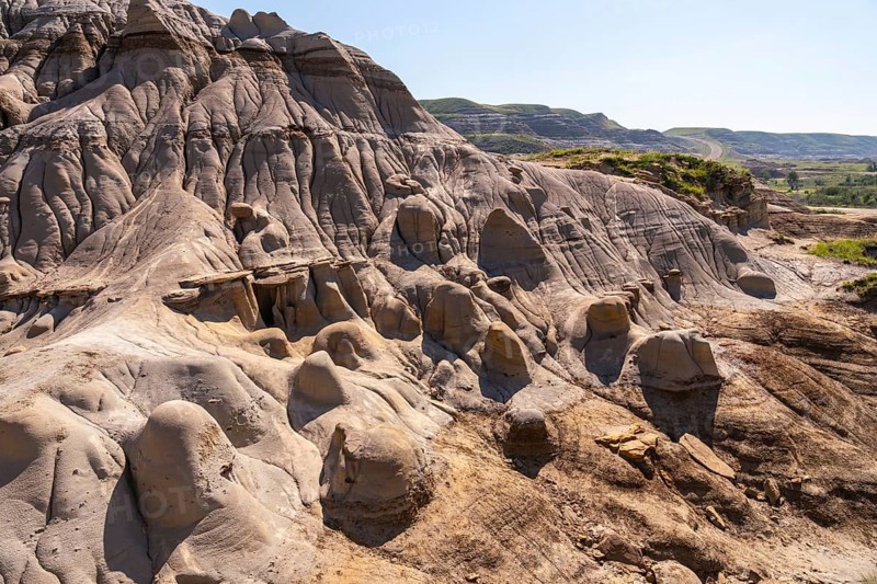 Sunlight illuminates the hoodoo badlands in drumheller, canada, showcasing unique rock formations and creating a dramatic landscape under a clear blue sky