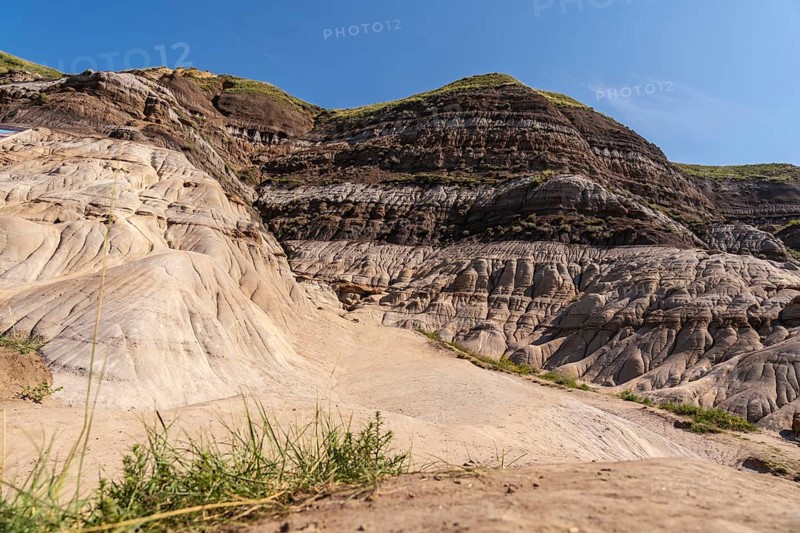 Sunlight illuminates the unique geological formations known as hoodoos, rising from the dry ground in drumheller, alberta, showcasing the beauty of the canadian badlands on a clear day