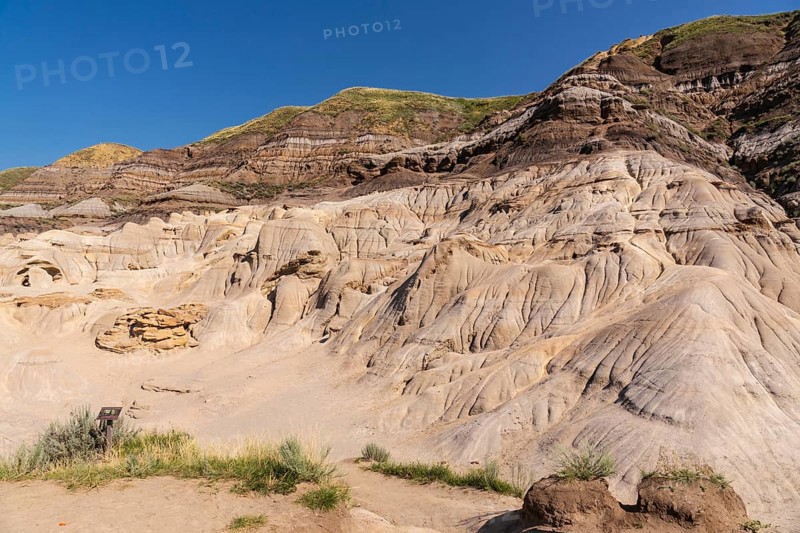 Sunlight bathes the otherworldly terrain of drumheller, alberta, showcasing the unique hoodoo formations rising from the arid landscape under a vibrant blue sky