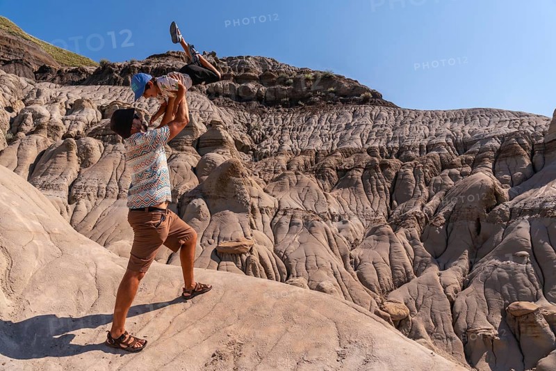 Father playfully lifting his son in the air at horseshoe canyon in drumheller, alberta, canada, enjoying a sunny day surrounded by unique geological formations
