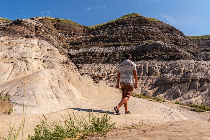 Tourist exploring the arid landscape of the canadian badlands, walking through the unique geological formations known as hoodoos in drumheller, alberta, on a sunny day