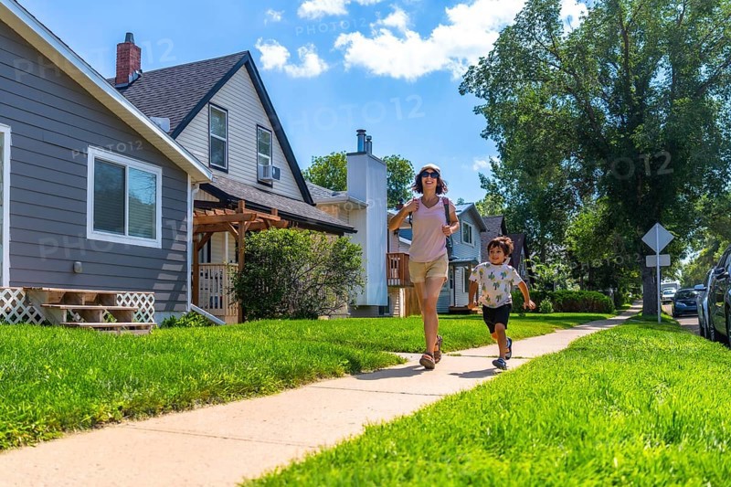 Mother and her young son are running on the sidewalk in a quiet, residential neighborhood on a sunny summer day, enjoying quality time together