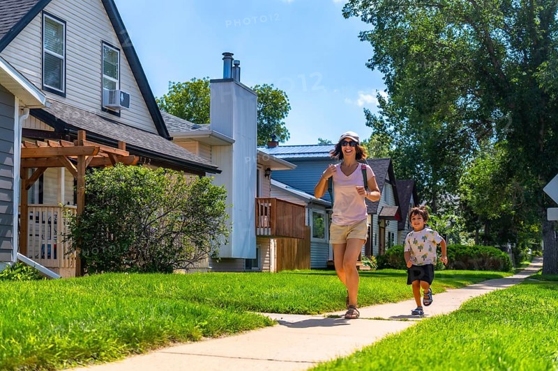 Mother and young son running joyfully on a sidewalk in a sunny, residential neighborhood, cherishing quality time outdoors while embracing a healthy, active lifestyle together