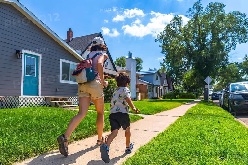 Mother with backpack and her son are running on the sidewalk in a residential area of drumheller, alberta, during a sunny summer day, showcasing the peaceful suburban life