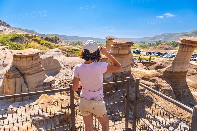 Young woman enjoying view of unique hoodoo rock formations at tourist attraction in drumheller, alberta, showcasing natural beauty and geological wonders of canadian badlands on sunny summer day