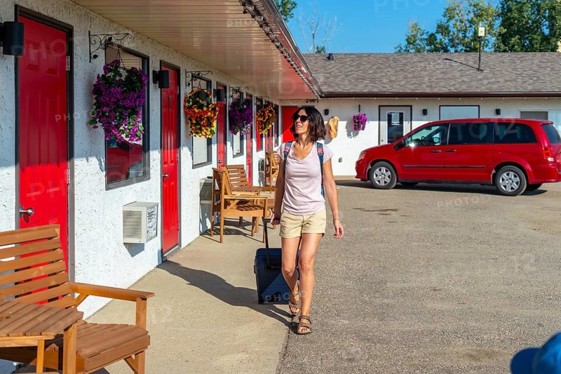 Female tourist pulling her luggage while strolling towards her room at a roadside motel, enjoying a sunny summer road trip vacation filled with adventure and exploration