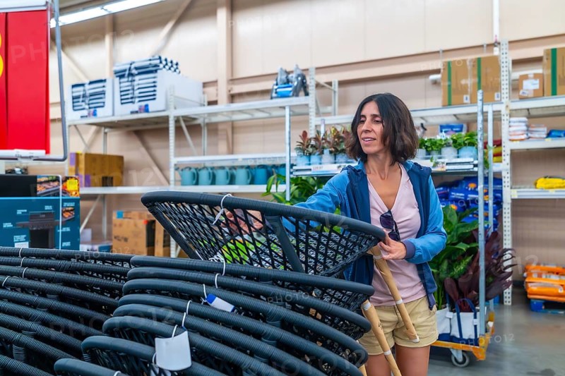 Smiling female customer selecting new outdoor furniture, picking up hanging egg chair in warehouse, shopping for home goods, enjoying weekend retail therapy