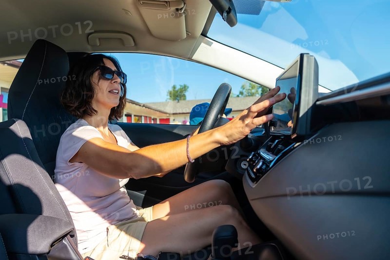 Woman wearing sunglasses driving a modern car and using gps navigation system on the dashboard touchscreen while holding the steering wheel