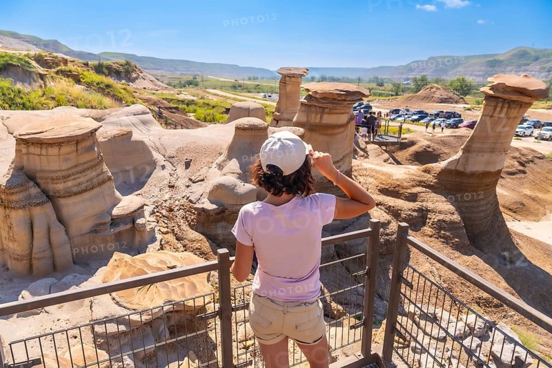 Young woman shielding her eyes from the sun while admiring unique hoodoo rock formations in drumheller valley, a stunning natural wonder in alberta, canada