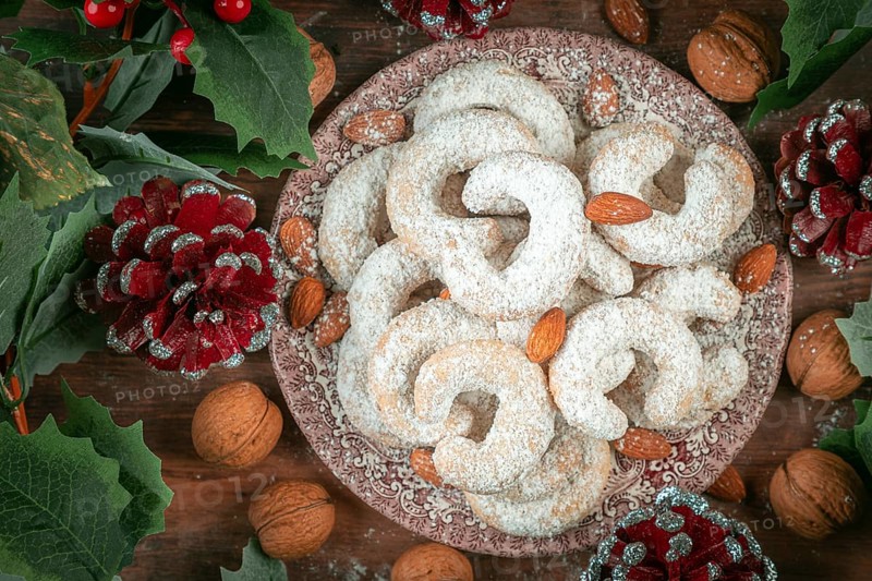 Vanilla croissants on a plate surrounded by walnuts, almonds and Christmas decorations