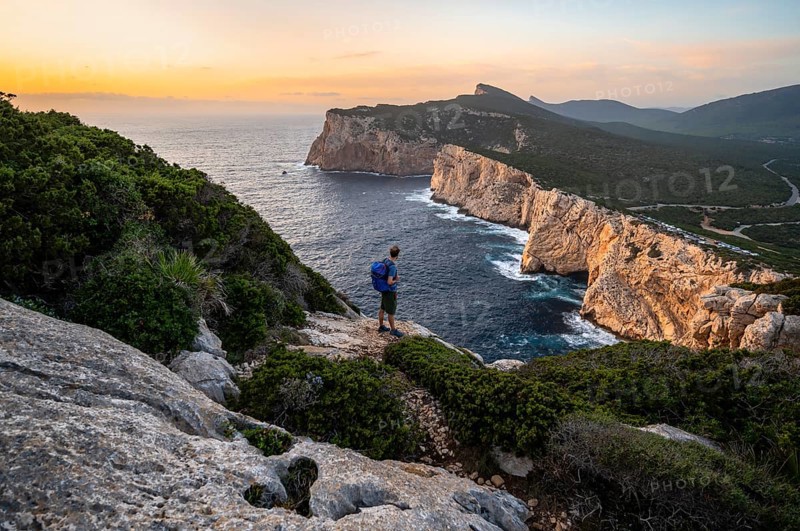 Tourist in front of coastal landscape at sunset, steep cliffs by the sea, cliffs in the evening light, Capo Caccia, Alghero, Sardinia
