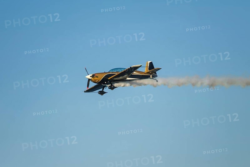Golden stunt aerobatic plane performing stunts in blue sky with smoke trail. Concept of speed, difficulty, precision, risk