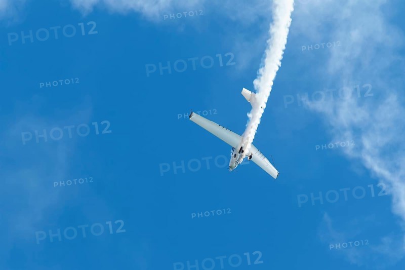 Stunt aerobatic plane performing stunts in blue sky with smoke trail. Concept of speed, difficulty, precision, risk, challenge