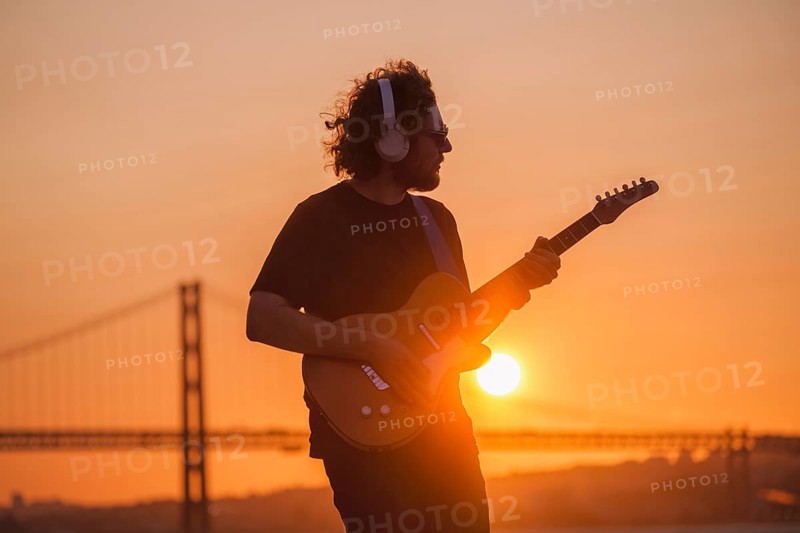 Hipster street musician in black playing electric guitar in street outdoors on sunset with lens flare and light leak