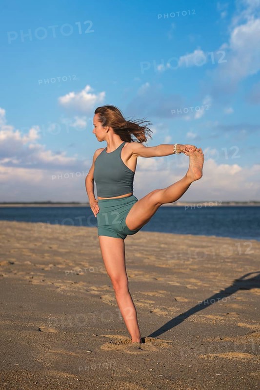 Woman yoga practice at the beach in Utthita Hasta Padangusthasana Extended Hand-to-Big-Toe Pose pose