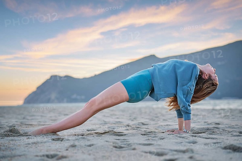 A woman practices Purvottanasana, or upward plank pose, on the beach during sunset. The golden sky reflects on her focused core work as she balances on the sand in serene surroundings