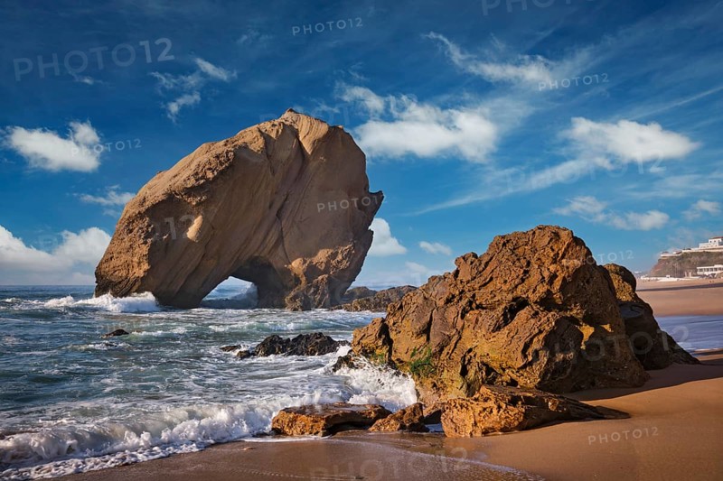 Penedo do Guincho rock at Praia da Santa Cruz as waves crash against the sandy shore during a colorful sunset