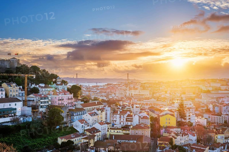 Breathtaking sunset over Lisbon, highlighting the city's rooftops, Carmo Convent ruins, and the iconic 25th of April Bridge. Portugal