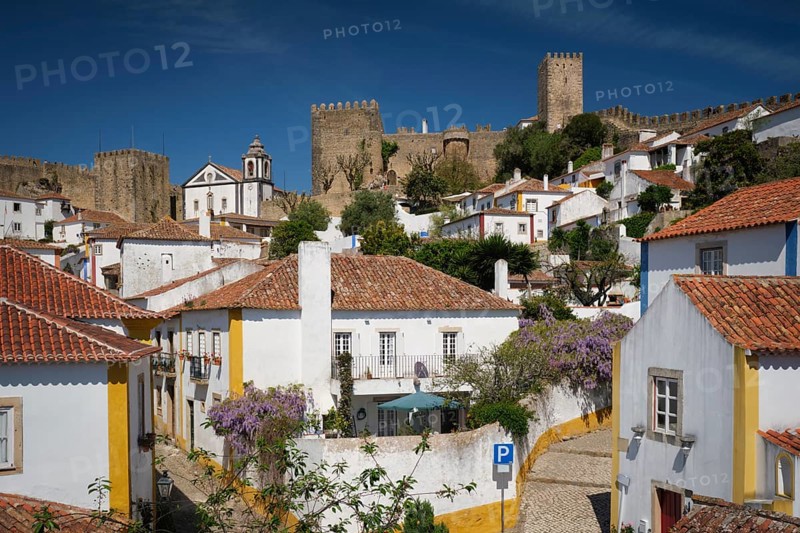 Obidos town featuring white houses, vibrant rooftops, and the impressive medieval castle under a blue sky. Portugal