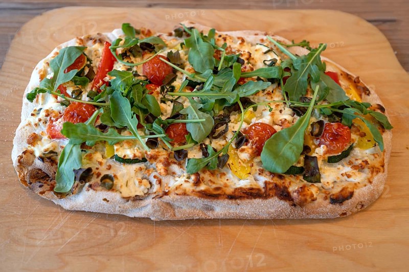 Pizza with goat cheese, tomatoes and arugula served on a wooden board, Ahrenshoop, DarÃŸ, Mecklenburg-Vorpommern, Germany