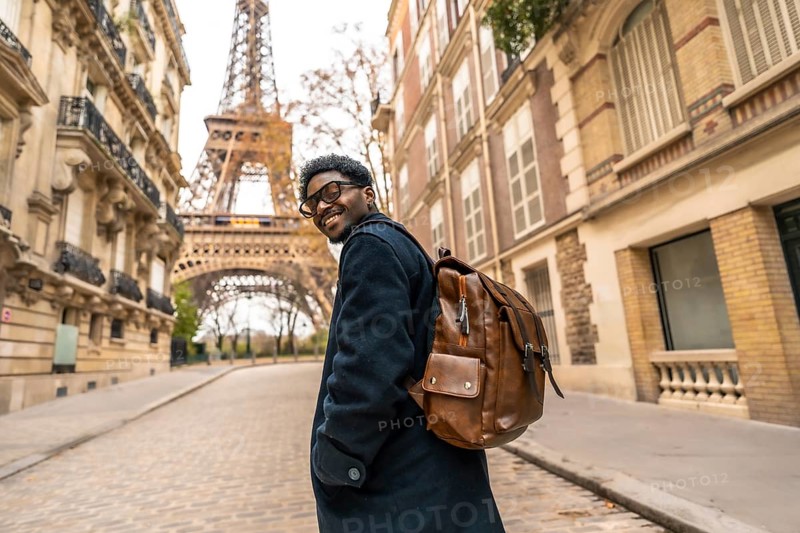 Young man smiling and turning back while exploring a historic street in paris, enjoying his leisure travel with the iconic eiffel tower visible in the background