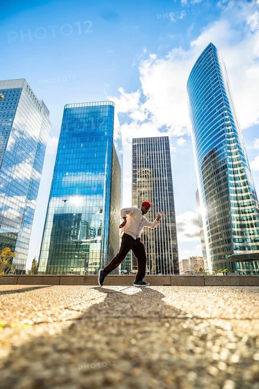 Man running with energy and freedom against a backdrop of modern glass skyscrapers, symbolizing progress, future, and the dynamic pace of urban life under a bright sky