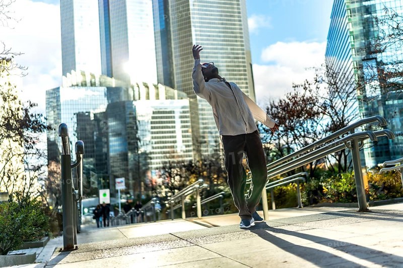 Man finding personal freedom and expressing himself through expressive urban dancing on a public stairway in a modern city against a bright sky and contemporary architecture during daylight