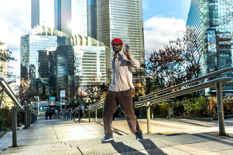 Man with red hat and sunglasses walking down an outdoor staircase in a modern central business district, expressing urban lifestyle and confident attitude