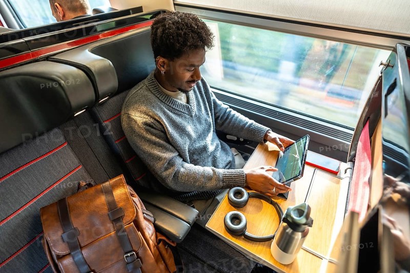 Young man traveling by high speed train, staying productive by working on a digital tablet at his seat, combining comfort and efficiency for modern business travel