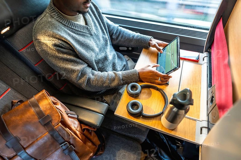 Man finding comfort and productivity while traveling for business, utilizing his tablet and staying connected during a train journey with a window view