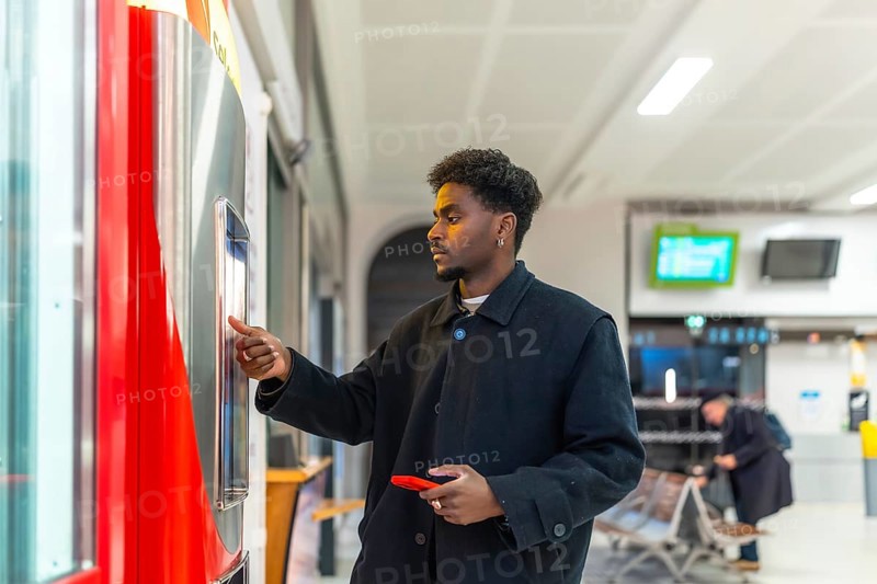 Young businessman standing at a train station, purchasing a ticket from an automatic vending machine for his upcoming business trip using public transport