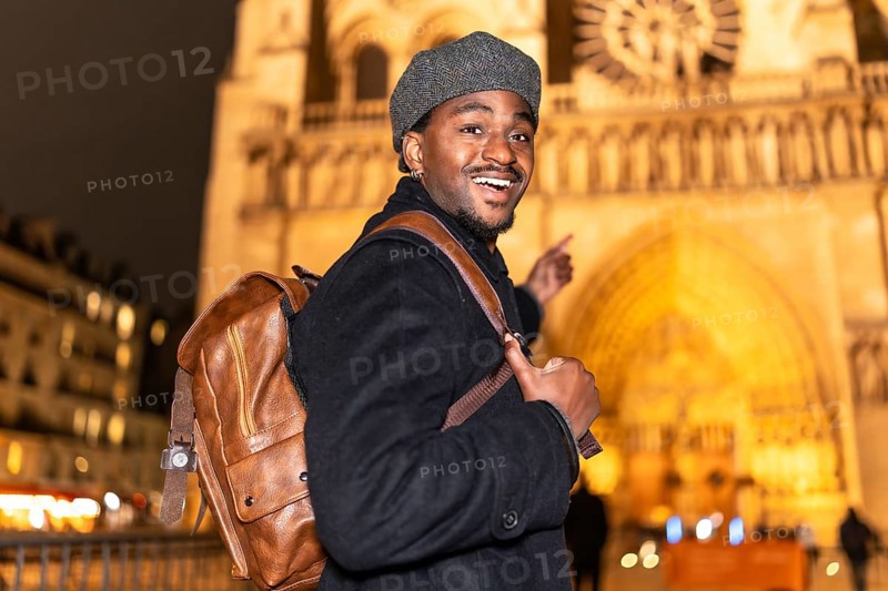 Young african american man smiling and pointing, enjoying a night out in paris and exploring an illuminated historic building during his trip to france