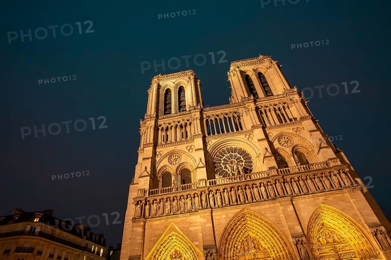 Notre dame de paris cathedral showcasing its historic gothic architecture and intricate details, bathed in warm golden light against a deep blue evening sky, a symbol of french culture and travel
