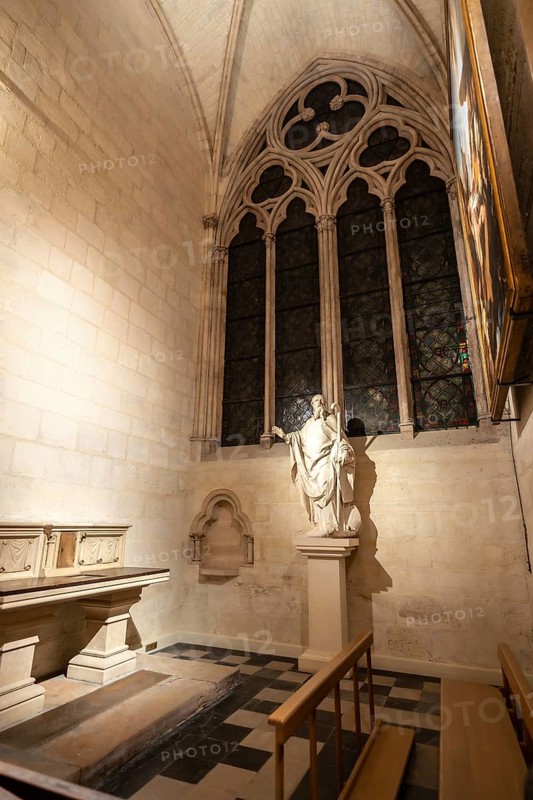 Gothic chapel interior featuring a statue of a saint, an arched window with detailed tracery, and checkered floor, highlighting the rich religious history and architectural beauty